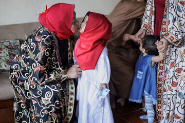 Grandmother kissing granddaughter during lebaran idul fitri day. 