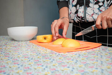 Manos de una mujer delgada cortando una manzana en una tabla de picar sobre una mesa con mantel de...