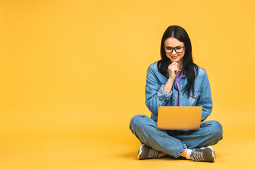 Business concept. Portrait of happy young woman in casual sitting on floor in lotus pose and holding laptop isolated over yellow background. - 512840581