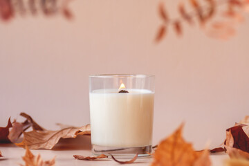 Burning vanilla candle on beige background. Warm aesthetic autumn composition with and dry leaves...