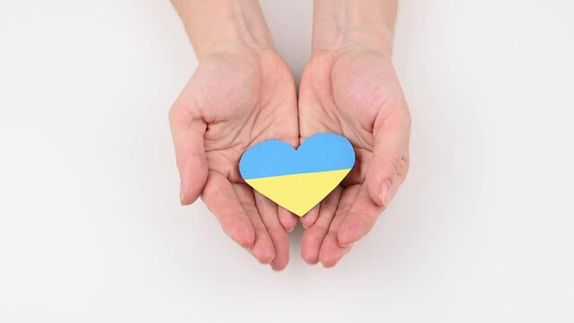 Woman opens her palms with a heart with the flag of Ukraine. 