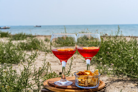 Two glasses of an Italian appetiser Gingerino drink with dry fruits snack on the beach with sea coast view