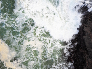 Top view of the raging ocean. White foamy waves crash against the shore. Abstraction. Minimalism. Wildlife beauty, environmental protection, geology, weather, extreme sports.