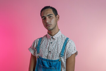 Young trendy Hispanic Latin gay man 20s with make-up in a fashionable bright shirt isolated on pink...