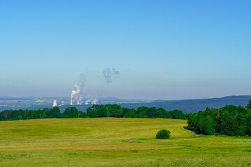 Green scenery of hilly landscape with distant coal power plant