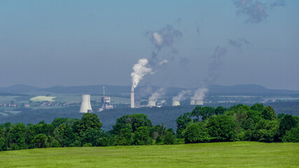 Chimneys of carbon power plant emitting carbon dioxide to the air in the background of the forest trees