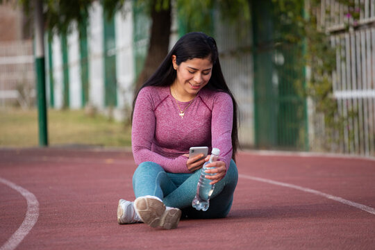 Mujer deportista revisando su teléfono sentada en una pista atlética. Concepto de personas y estilo de vida.