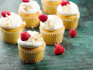 Many muffins with cream, raspberries and almonds on a dark green background. Holiday, banquet, picnic. Holiday invitation, advertisement, banner. There are no people in the photo.