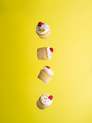 Appetizing little muffins with whipped cream and fresh raspberries on a bright yellow background in frozen flight. There are no people in the photo. Birthday invitation, advertisement, banner.