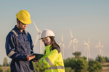 Two engineers working and holding the report at wind turbine farm Power Generator Station on mountain,Thailand people,Technician man and woman discuss about work