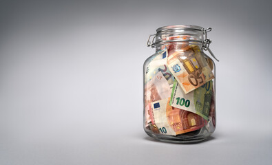 Glass jar with euro currency savings on grey background