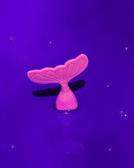 Fish in sea concept. Pink tail on purple background. Mermaid symbol.
