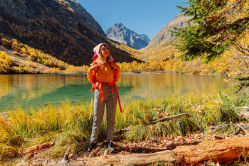 Happy woman with backpack at lake in the autumnal mountains. Mountain lake and tourist
