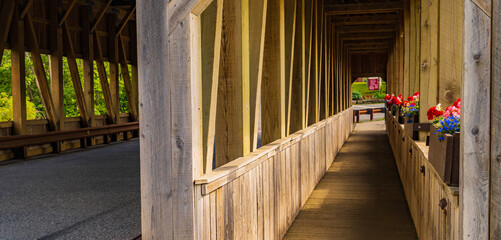 through a historic covered bridge along pedestrian walkway with flower boxes in bloom
