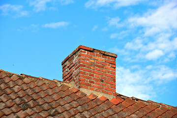 Red brick chimney designed on slate roof of a house building outside with cloudy blue sky...