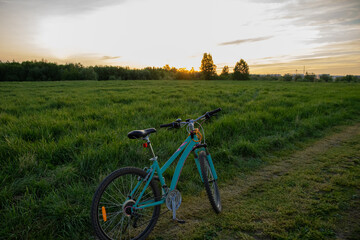 Fototapeta na wymiar A woman's bicycle stands in a green field with grass and trees at sunset, on the outskirts of the city.
