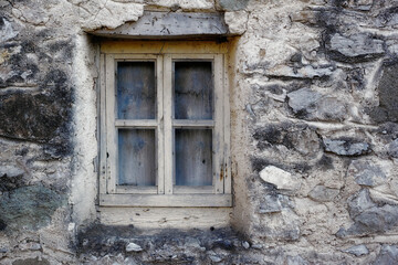 Closeup of a wooden frame window on ancient house in a village. Exterior of old dirty window and wall on farmhouse. A small window and grey stone or brick wall of an old antique building or cottage