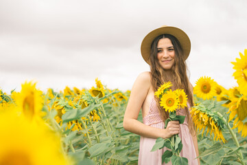 young caucasian woman with a dress and straw hat in a field of sunflowers with a bouquet of...