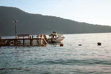 Lonely fishing boat moored at a wooden pier facing the horizon on calm waters in the late afternoon. Maguariquessaba Beach, Ilha Grande, Angra dos Reis, Rio de Janeiro, Brazil.