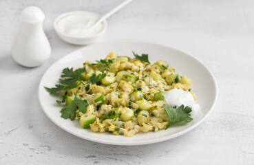 Turkish scrambled eggs with zucchini served with yogurt on a light blue background. Delicious homemade vegetarian food