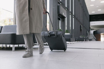 woman at the airport or congress center with a suitcase is sitting in the waiting area and chatting on her smartphone. a beautiful European woman in a beige trench coat at the airport is waiting to