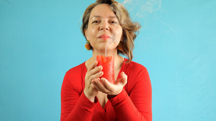 A forty-year-old woman in a red sweater holds a red candle on a blue background. Woman's magic. fantasy