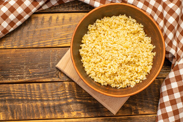 Cooked bulgur porridge in a clay bowl on a wooden table. Bulgur, a cereal made from wheat grains.. Top view, space for text, copy space