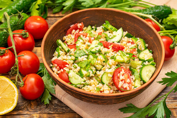 Tabbouleh salad is a traditional Middle Eastern or Arabic cuisine. Vegetarian salad with bulgur, tomatoes, cucumbers, parsley, lemon juice. Tabbouleh close-up on a background of fresh vegetables