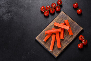 Crab sticks on a cutting Board with a knife. On black concrete background © chernikovatv