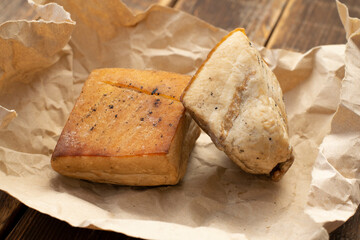 Two pieces of homemade smoked bacon in paper on a wooden table. Smoked lard with a layer of meat close-up.