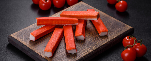 Crab sticks on a cutting Board with a knife. On black concrete background © chernikovatv