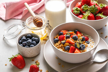 Homemade granola with yogurt or milk, blueberry, strawberry and honey in bowl on grey background....
