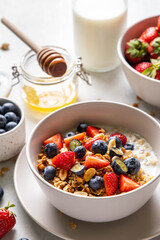 Homemade granola with yogurt or milk, blueberry, strawberry and honey in bowl on grey background. Healthy breakfast. Selective focus.