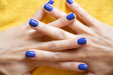 Manicure and blue polish on the girl's finger on a yellow background, yellow-blue color of the flag of Ukraine, gel polish on the girl's nails