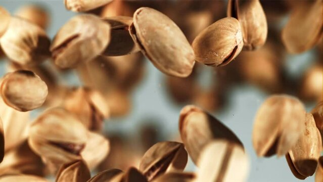 A pile of pistachios rises up and falls down. On a blue background. Filmed on a high-speed camera at 1000 fps.