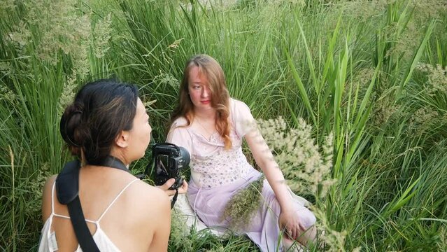 Spring photo shoot for a cute girl in white dress. Cheerful young white woman with long hair at the camera among the grass in the park on sunny day. Video for memory.