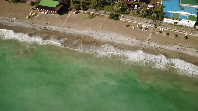 Drone aerial view of a coastal resort beach with gentle waves washing the shoreline, turquoise sea water and relaxing summer vacation atmosphere.