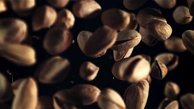 Pistachios rise up and rotate in flight. Top view. On a black background. Filmed is slow motion 1000 fps.