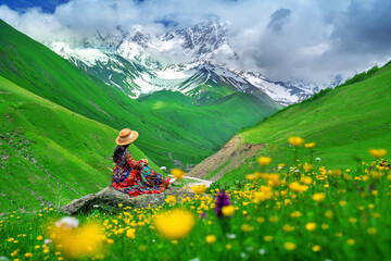 Tourist sitting on the rock at green pasture against highest georgian mountain Shkhara near Ushguli...