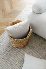 Wicker basket with cushions standing on rug, near sofa