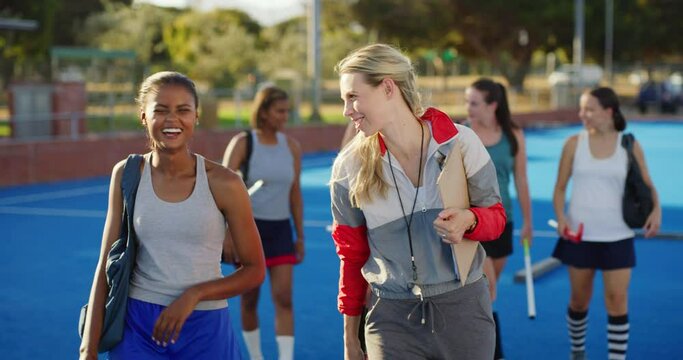 Playful female hockey coach talking to a young girl player after practice. Hockey player walking with her PE teacher as having an interesting pep talk during training outside on the sports court