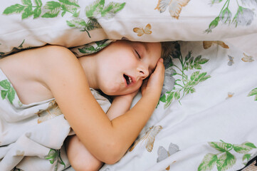 A beautiful little girl with long hair, a preschool child of five years old, sleeps on a large bed, covered with a warm blanket. Photography, concept.