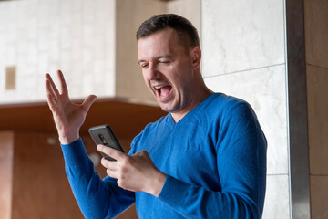 Overjoyed surprised middle aged man standing in hall, using cellphone, receiving good news, emotional reaction. Portrait of excited student receiving good news on phone in university hallway.