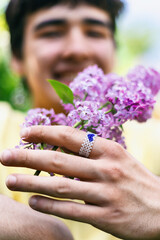 heart-shaped ring on the finger of young man holds lilac flower, LGBT theme, bisexual man