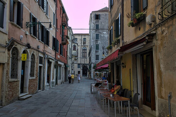 Venice, Italy: Small outdoor restaurant with red tables and chairs on narrow street - is one of the many bars and restaurants popular with tourists in the evening hours on street
