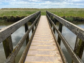 Beautiful landscape with wood bridge over waterway with reeds and sand path at nature reserve by the beach on East Anglia uk coastline at Walberswick Suffolk on Summer day with blue sky white cloud