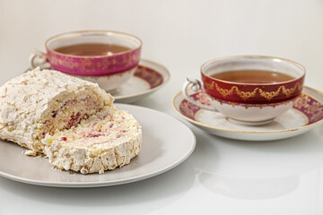 delicious meringue roll with strawberry cream and vintage cups of tea on a white glass surface