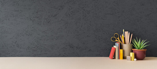Creative desk with a blank picture frame or poster, desk objects, office supplies, books, and plant on  grey wall background.