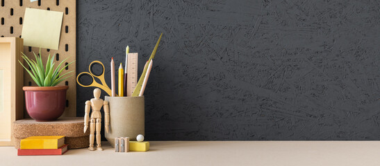 Creative desk with a blank picture frame or poster, desk objects, office supplies, books, and plant on a grey background.