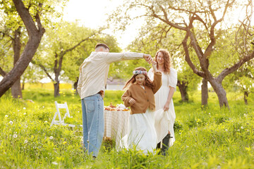 Happy family on holiday vacation. Mom, dad and little girl relax and enjoy with dinner party together in the green park at summer sunset. mothers, fathers and babies day.